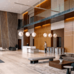 Modern lobby with high ceilings, seating areas, a marble reception desk, and two people present.