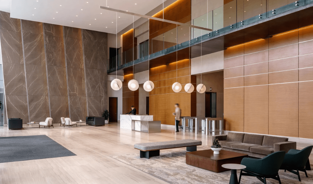 Modern lobby with high ceilings, seating areas, a marble reception desk, and two people present.