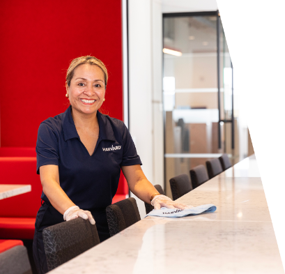 _TP_3418 (1)-1 (1) A woman in uniform cleans a countertop in a modern, red-accented office or cafeteria setting.
