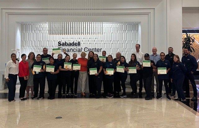 A group of people stand indoors holding certificates at Sabadell Financial Center.