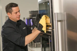 Corporate-cleaning-company A technician wearing black gloves cleans a microwave with a yellow cloth.
