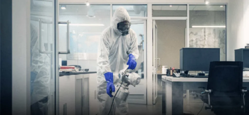 Harvard-janitorial-services Person in a protective suit and mask using a disinfectant fogger in an office.