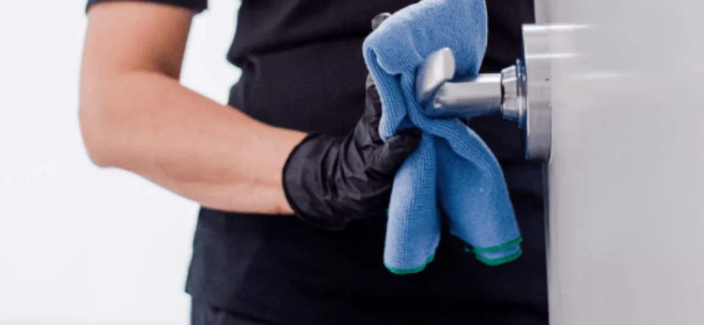 Janitorial-maintenance-companies A person wearing black gloves wipes a door handle with a blue cloth.